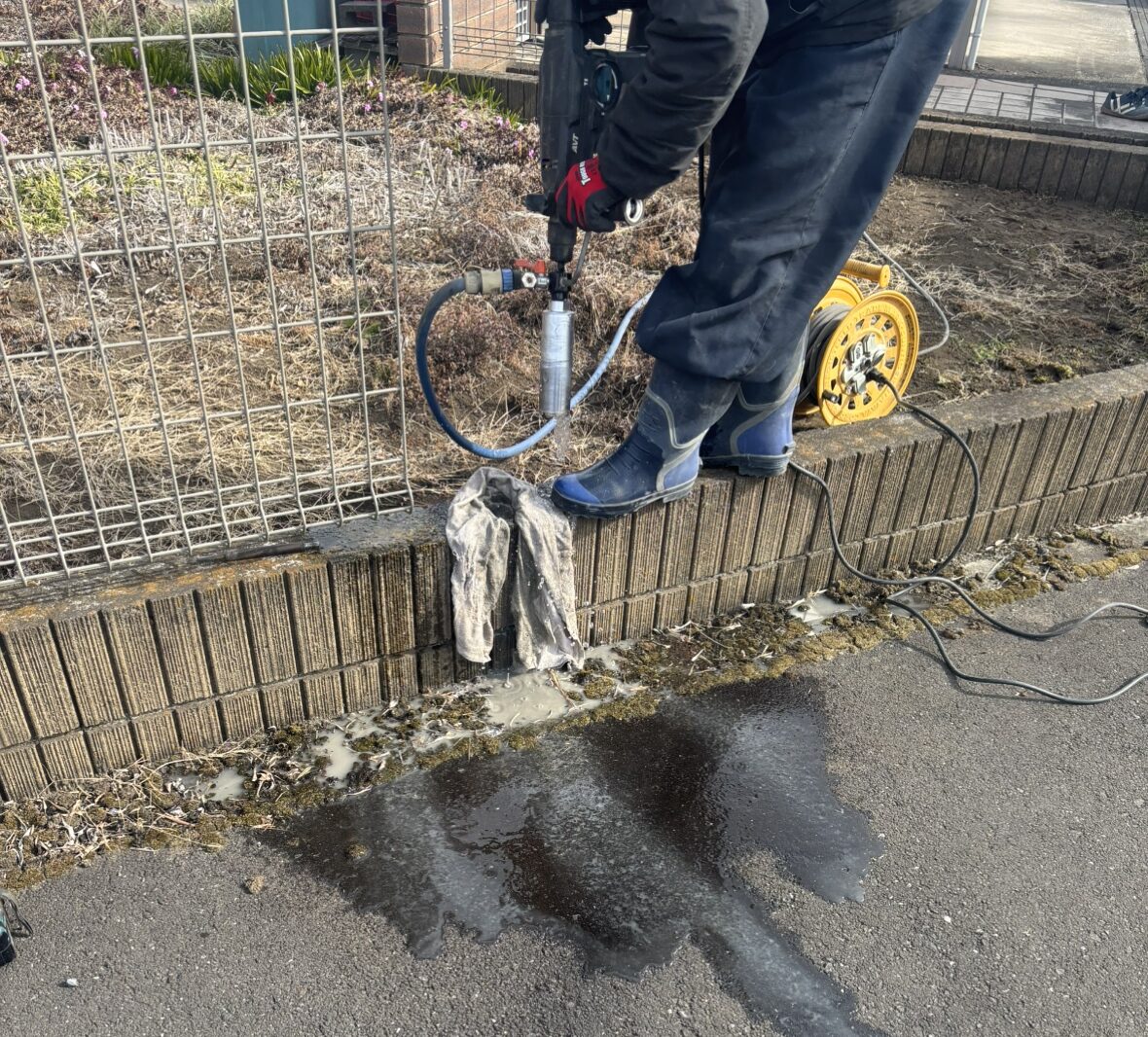 フェンス改修工事の既存のフェンスの柱を撤去した後に新設の柱を設置する為にコア穴明けの作業となります。